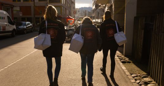 Drei Open Heart Helferinnen mit Taschen voller Verpflegung, unterwegs zu obdachlosen Menschen auf Zürichs Strassen.